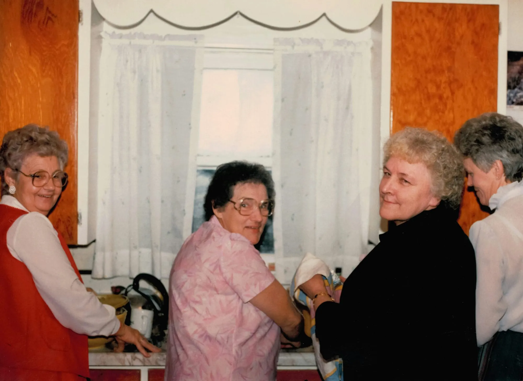 Vintage photo: several older women laughing together in a kitchen.